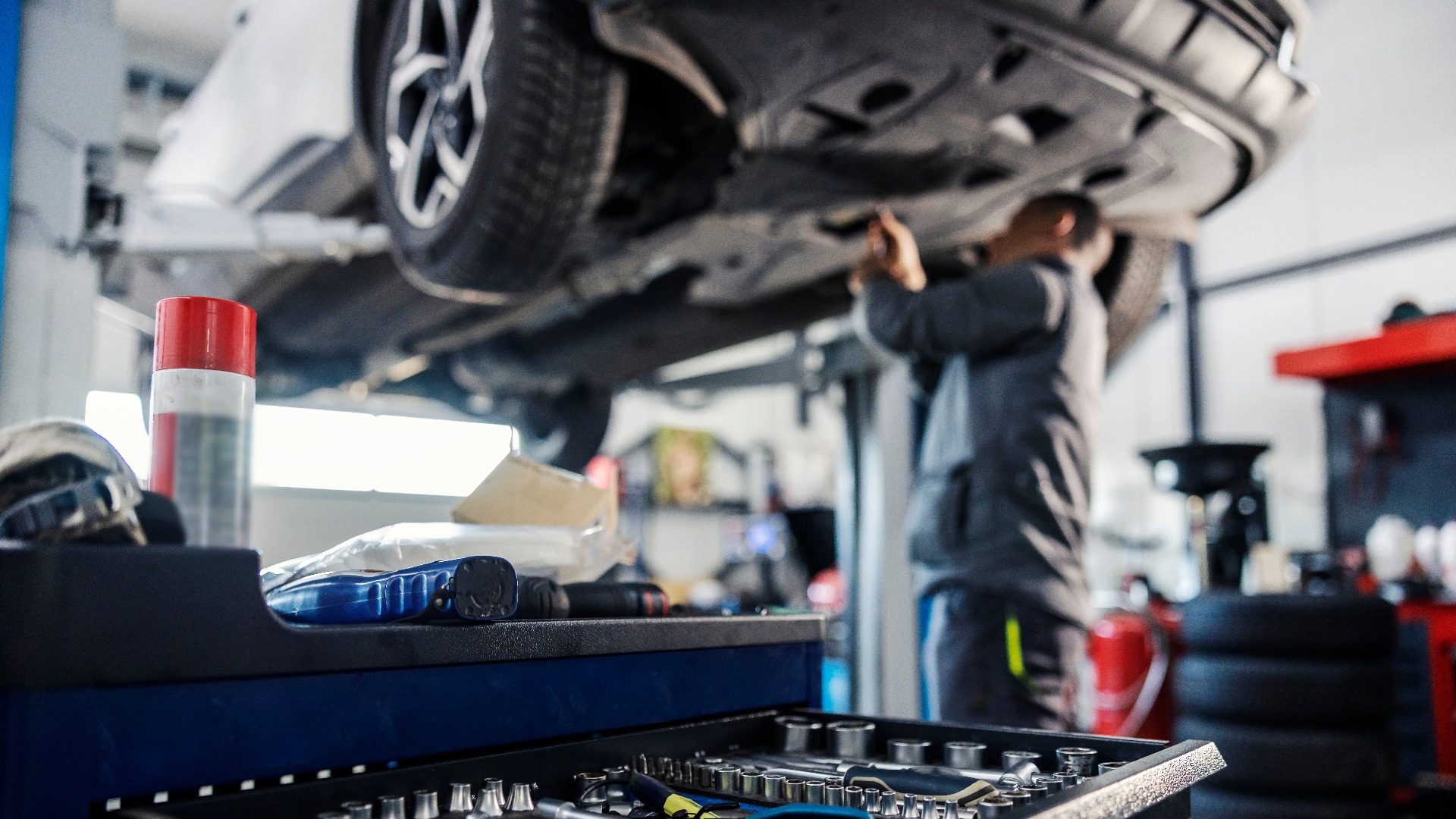 Selektiver Fokus auf ein Werkzeug im Werkzeugkasten in einer Werkstatt mit einem Mechaniker, der das Auto im unscharfen Hintergrund repariert.
